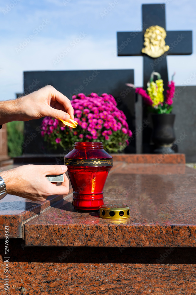 The All Saints' Day at the Christian cemetery, on a sunny day. A man lights a candle on a tombstone with a match.