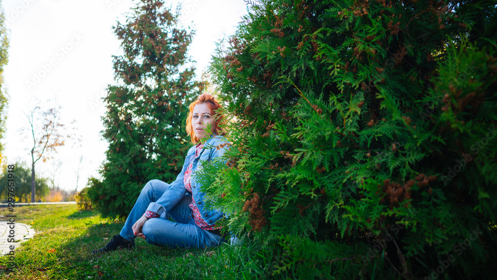 Young woman with red hair among trees. Portrait of young attractive female with trendy hairstyle standing in spring garden and looking at camera Young woman with red hair among trees. Portrait of young attractive female with trendy hairstyle standing in spring garden and looking at camera