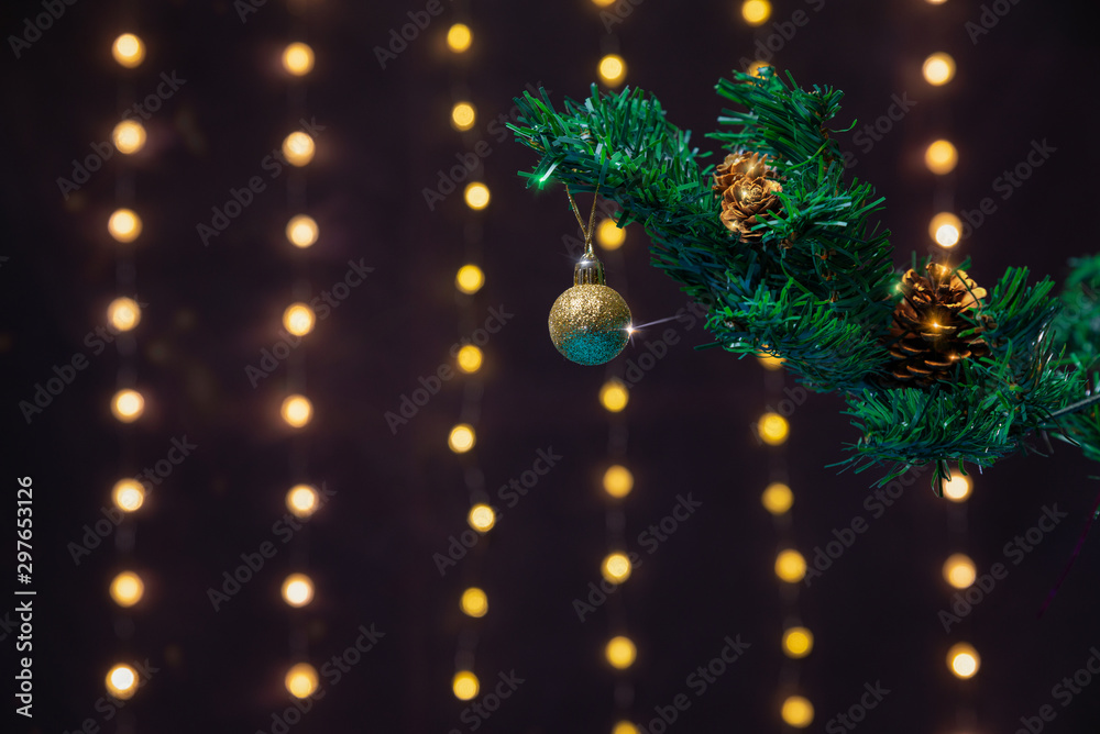 There is gold ball on the green xmas tree branch. There are glowing lights/bokeh and on the background. Merry Christmas. Happy New Year 2020. 