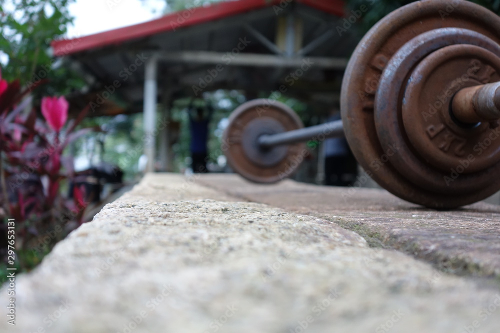 Rusty barbell lying on concrete infront of a small outdoor gym in nature Rusty barbell lying on concrete infront of a small outdoor gym in nature