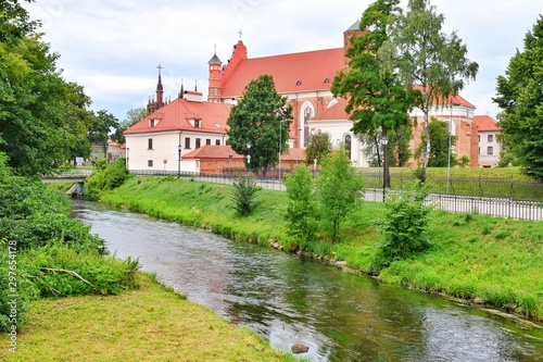 Lithuania, Vilnius - July 2019. An old brick cathedral with red roof tiles stands on the picturesque banks of the river in Vilnius. Old town. Lithuanian architecture. Town cityscape. 