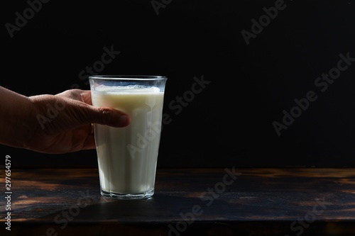 A hand grabbing and holding a glass of white milk in front of a black background