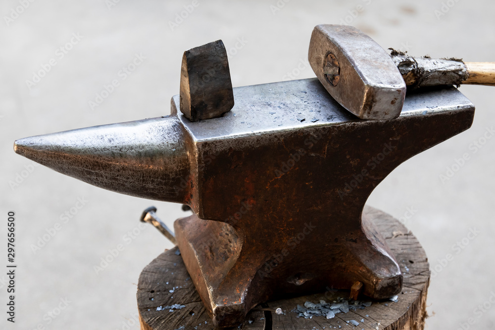 A hammer and a metal object on an anvil. Tools and metal objects used by  the blacksmith in a blacksmith shop. Photos | Adobe Stock