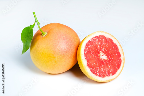 Close up image of juicy organic whole and halved grapefruits with green leaves & visible core texture, isolated background, copy space. Macro shot of bright citrus fruit slices. Top view, flat lay.