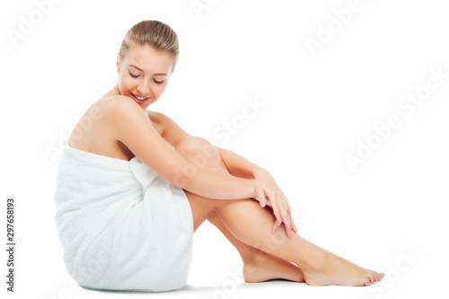 Beautiful young woman in white towel sits sideways to camera, on white background.