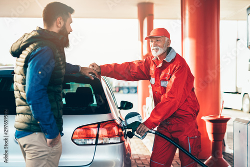 Young handsome adult man together with senior worker standing on gas station and fueling car.