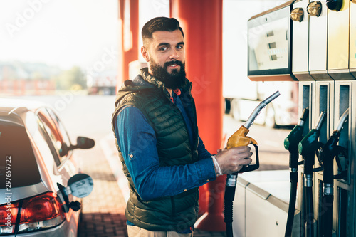 Obraz na płótnie Young handsome adult man standing on gas station and fueling his car