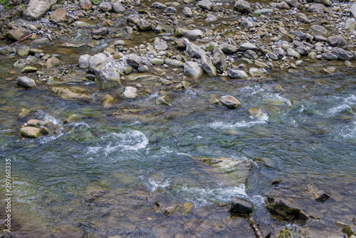 Beautiful mountain river with a fast flow. Large stones with rocks in the middle of a green forest.