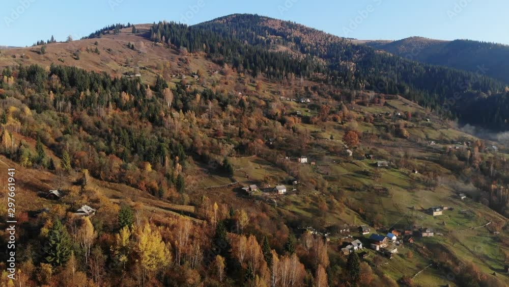 mountain village rare houses on green slope meadow surrounded by dense autumn forests lit by sunlight aerial view. Carpathian mountains, Ukraine beauty nature. Travel, autumn holidays. 4K mountain village rare houses on green slope meadow surrounded by dense autumn forests lit by sunlight aerial view. Carpathian mountains, Ukraine beauty nature. Travel, autumn holidays. 4K