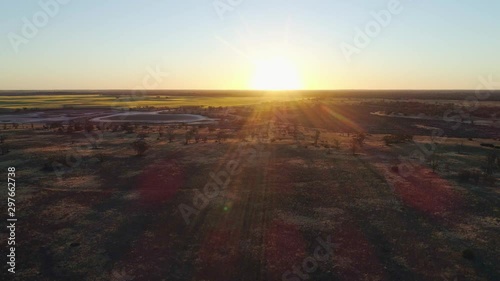 Aerial descend over Australian desert facing the setting sun with lens flare