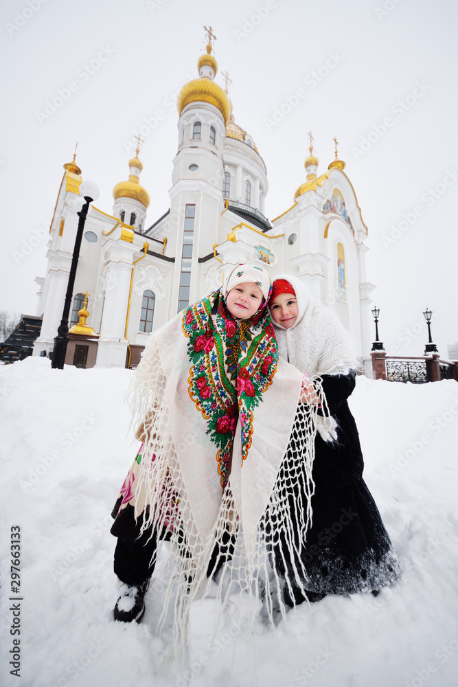 Two little girls in fur coats and shawls in Russian style against the background of a Christian church