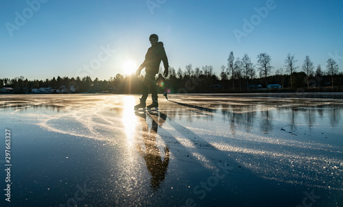 Fotografie Two silhouettes: teenage boys are ice skating on the crystal clear frozen lake i
