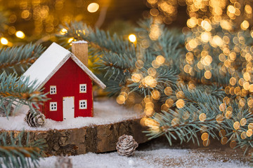 Miniature wooden house on the snow over blurred Christmas decoration background, toned