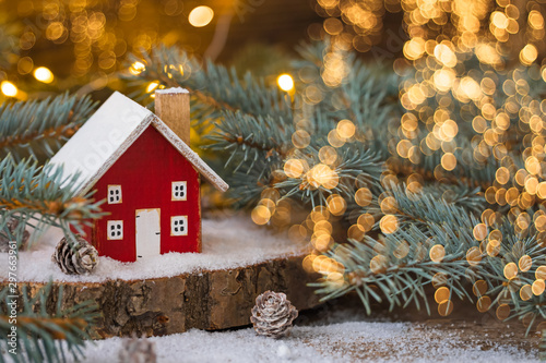 Miniature wooden house on the snow over blurred Christmas decoration background, toned