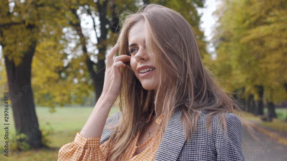 Smiling Caucasian girl putting on checkered jacket and looking away. Nice brunette woman in mustard dress with tweed print standing in the autumn park. Smiling Caucasian girl putting on checkered jacket and looking away. Nice brunette woman in mustard dress with tweed print standing in the autumn park.