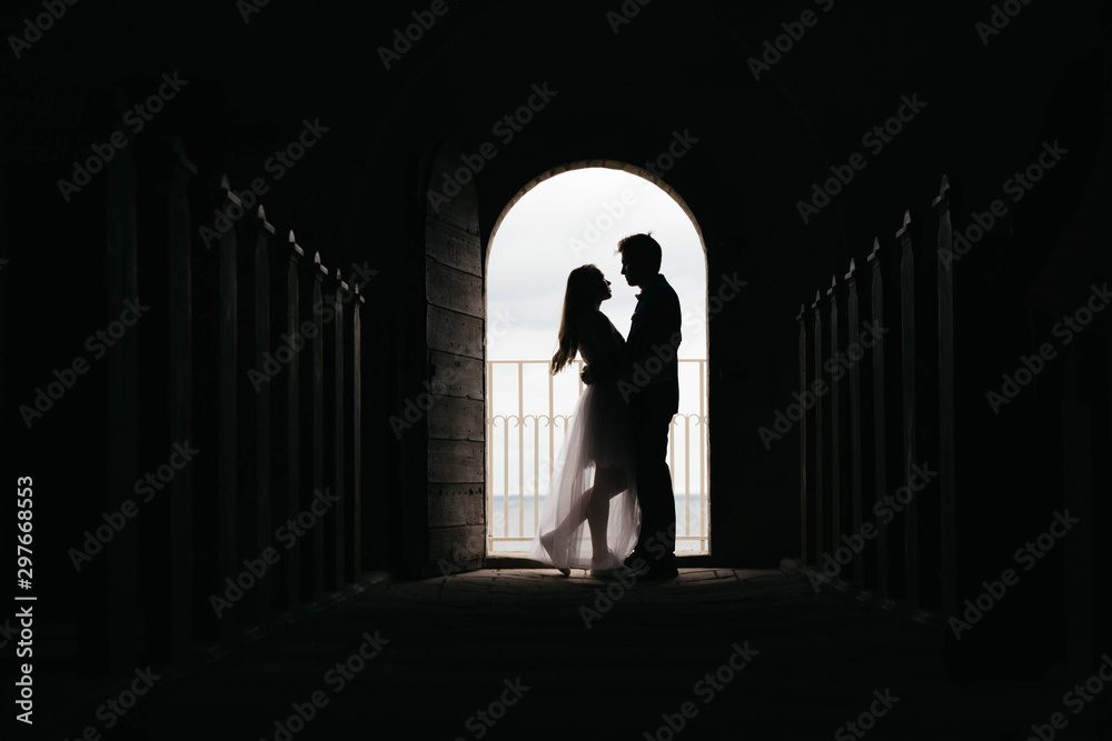 Silhouette of loving couple hugging while standing in doorway on black background, Bride and groom in wedding day posing in a doorway