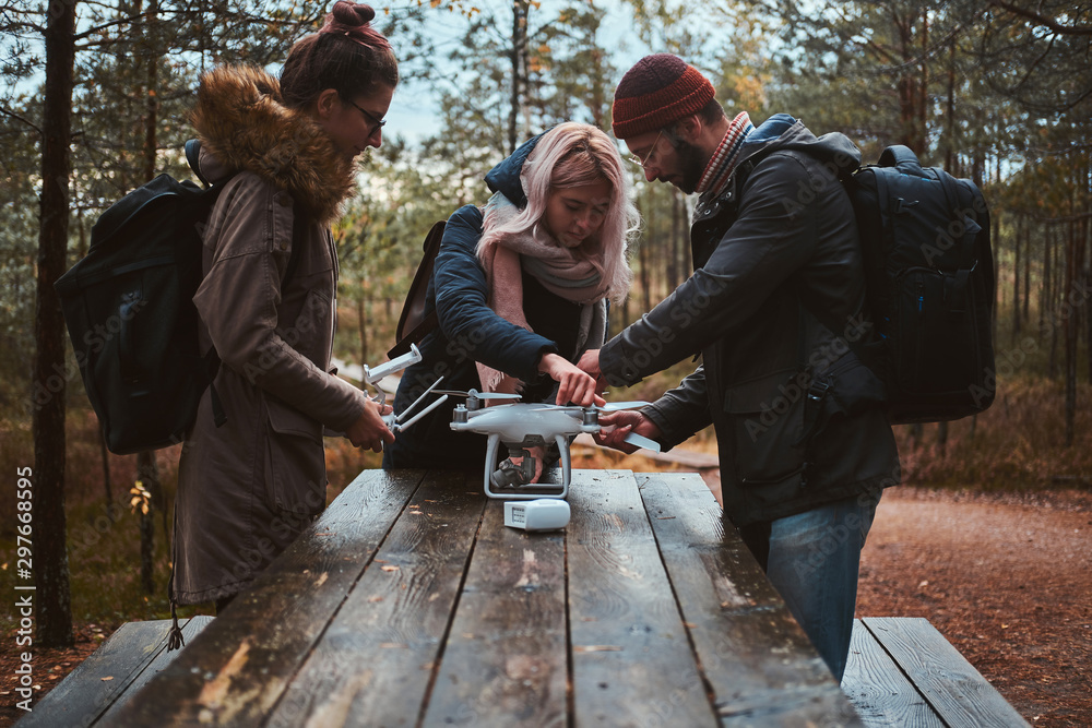 Small group of friends are assembling drone in the forestal park using wooden table. Small group of friends are assembling drone in the forestal park using wooden table.