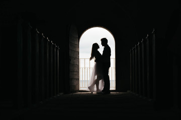 Silhouette of loving couple hugging while standing in doorway on black background, Bride and groom in wedding day posing in a doorway