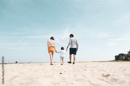 Back view of Asian happy family with a cute toddler having good time walking together on the tropical beach in the summer vacation, concept of family outing, Happytime of family on the beach.