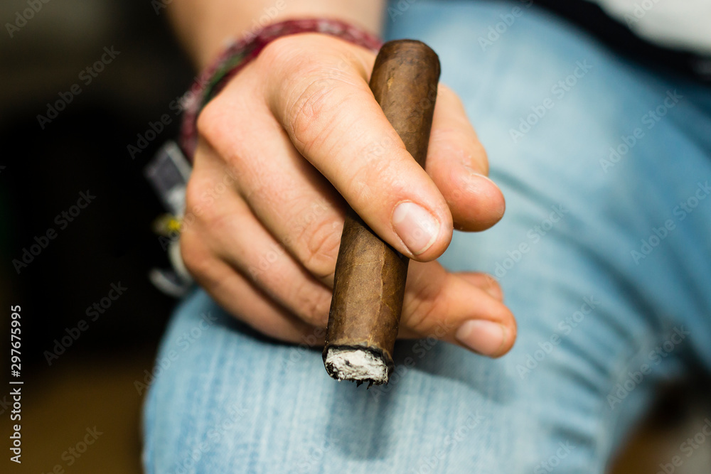 Lit cigar held in mans hand on jeans
