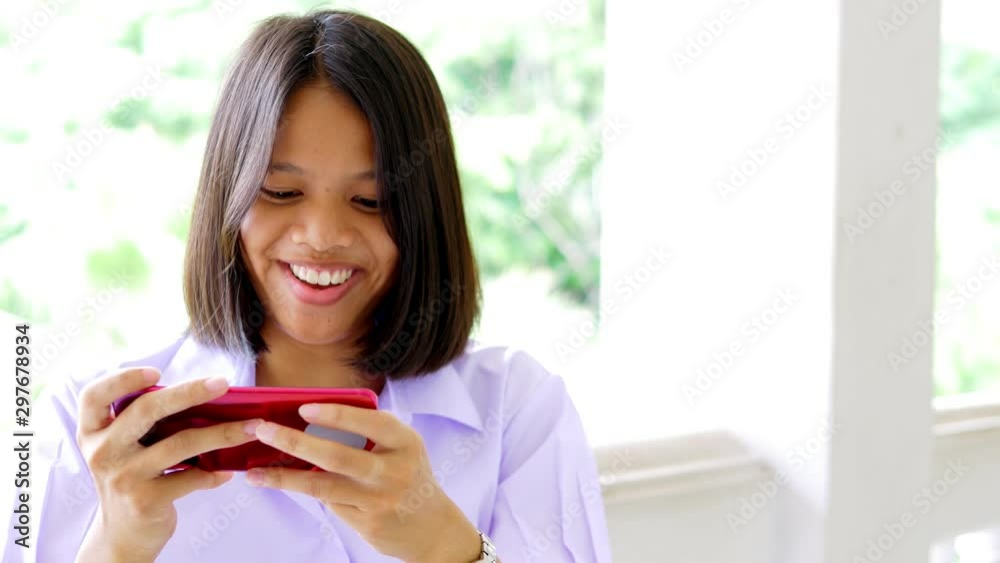 Asian female high school student in a white uniform, who is a lot of addicted to games, is playing exciting games on her mobile phone. Asian female high school student in a white uniform, who is a lot of addicted to games, is playing exciting games on her mobile phone.