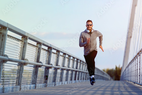 Fototapeta Naklejka Na Ścianę i Meble -  Attractive fit man running fast along big modern bridge. Exercising, Jogging, Sport, Winter. Male athlete running.