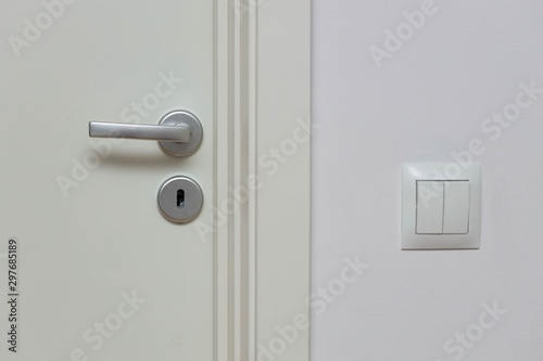 Close up view of silver door handle and white light switch isolated. Building construction elements concept.