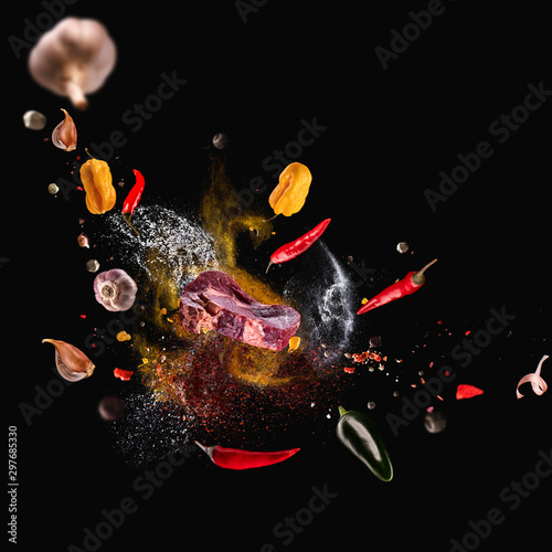 Fototapeta Naklejka Na Ścianę i Meble -  Hot red pepper, garlic, different spices powder meat stakes flying on a black background Motion freeze photo composition