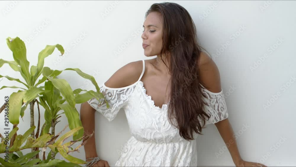 Happy brunette in white dress standing next to green plant Happy brunette in white dress standing next to green plant