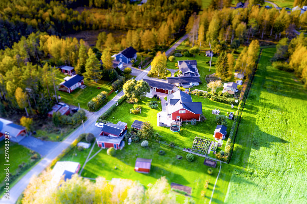 Tilt view photo of swedish village in Northern Sweden, red swedish wooden summer cabins surrounded by forest, green nature, sunny day, picture taken from a drone