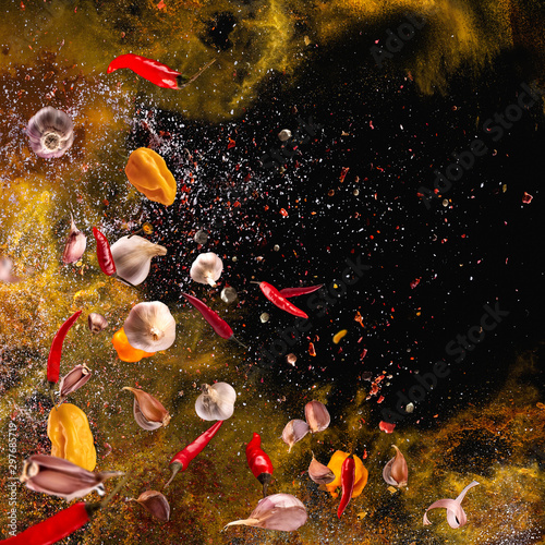 Fototapeta Naklejka Na Ścianę i Meble -  Hot red pepper, garlic, different spices powder flying on a black background Motion freeze photo composition