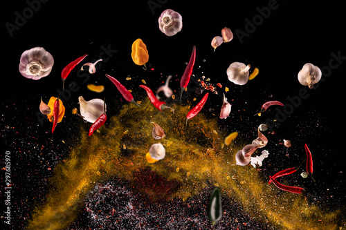 Fototapeta Naklejka Na Ścianę i Meble -  Hot red pepper, garlic, different spices powder flying on a black background Motion freeze photo composition