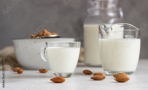 Organic almond milk in glass jugs with ingredients on a light grey background. Healthy and vegan eating. Alternative type of milk.