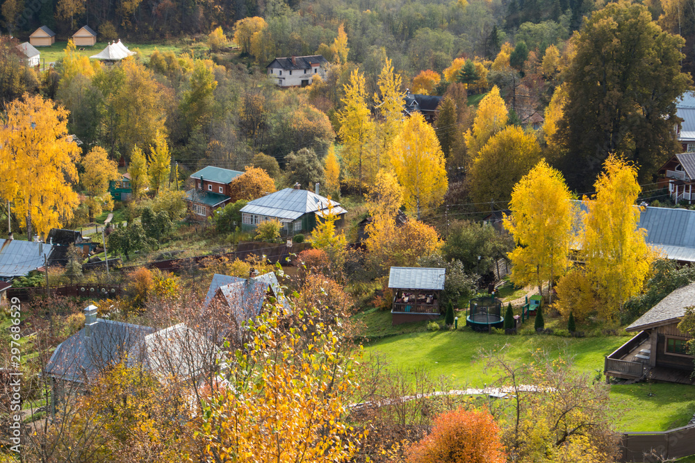 Fototapeta premium RUSSIA, Plyos - October 04, 2019: Ivanovo Region. Bright yellow autumn forest on background of Volga river. from height of Cathedral Mountain. Varvara church and colorful houses in autumn sunny day.