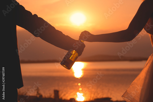 A couple is holding a bottle of wine in their hands with the sunsetin the background. What a romantic moment. photo