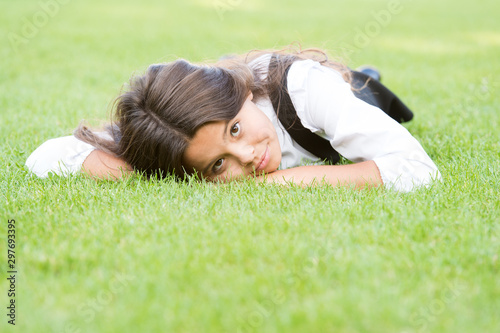 Lovely relaxed look. Adorable girl with school look relax on green grass. Cute little child have school look in formal wear. Vogue look of small fashion model