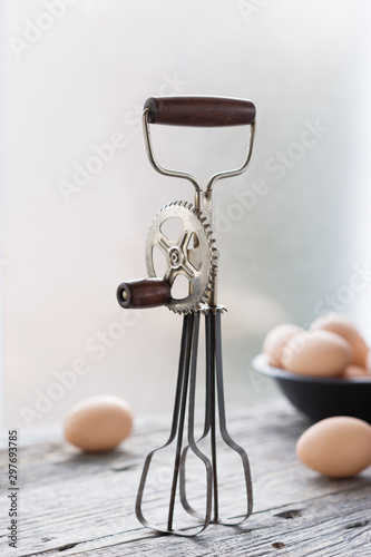 Obraz na plátně Manual egg beater and eggs on the wooden background.