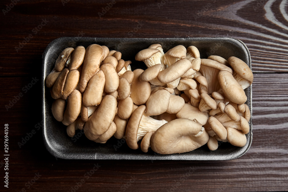 Oyster mushrooms in grey tray on wooden background, top view. Uncooked edible mushrooms on brown table, close-up Oyster mushrooms in grey tray on wooden background, top view. Uncooked edible mushrooms on brown table, close-up