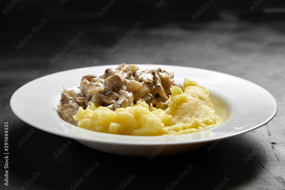 Mashed potatoes with fried oyster mushrooms in a white ceramic plate on a black stone table Mashed potatoes with fried oyster mushrooms in a white ceramic plate on a black stone table