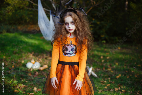Portrait of masked little girl in zombies, wearing Halloween orange costume. Children's party.