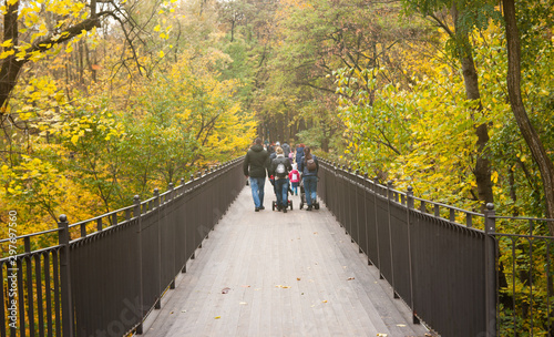 family walks on a foot bridge in the park in autumn