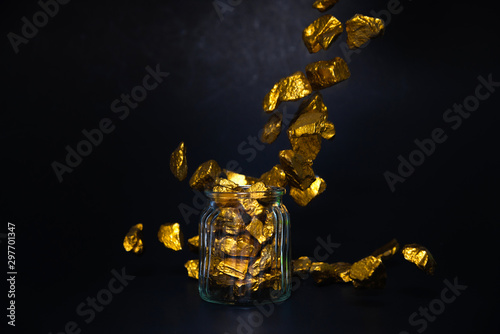 Falling gold nuggets or gold ore and glass jar in dark room