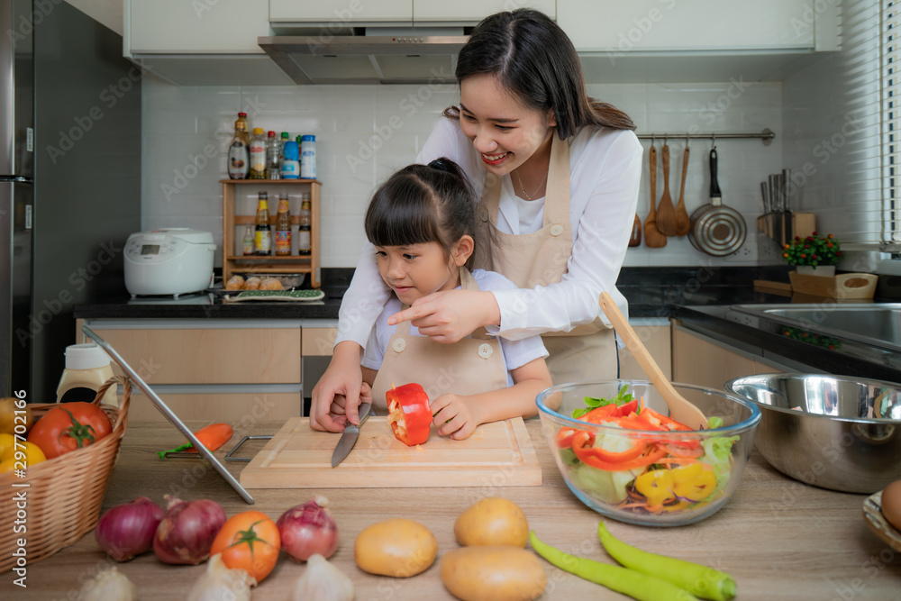Portrait of beautiful Asian young woman and her daughter cooking salad for lunch using online internet in a digital tablet search recipe while making food, Family life love relationship Portrait of beautiful Asian young woman and her daughter cooking salad for lunch using online internet in a digital tablet search recipe while making food, Family life love relationship