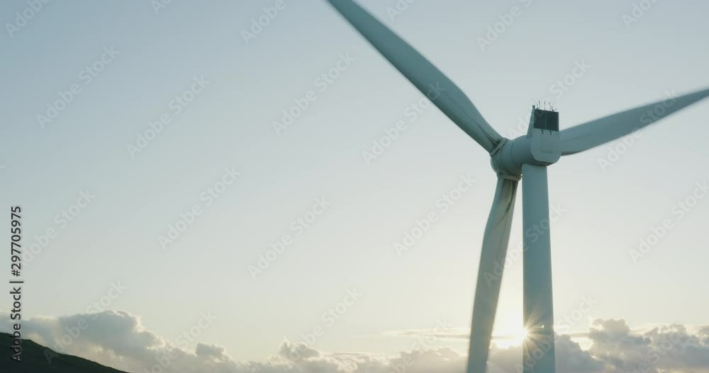 Aerial view of a windmill spinning with the sun rising behind it, green clean energy future concept
