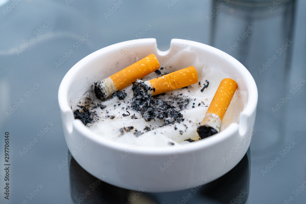 White dirty ashtray with cigarette stubs. Cigarette. White dirty ashtray with cigarette stubs. Cigarette.