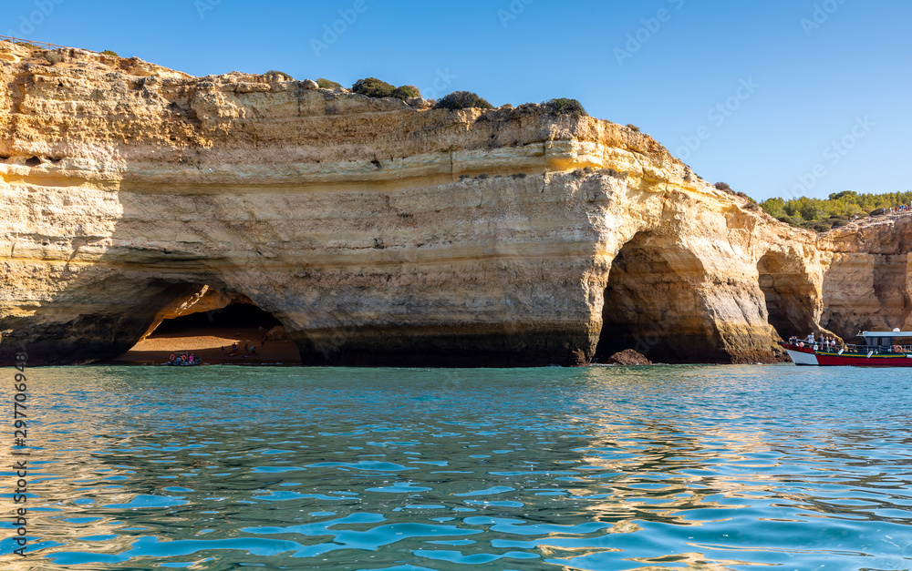 Landscape with the famous Benagil Caves, clear blue sky, sandstone cliffs and tour boat on the Algarve coast in Portugal