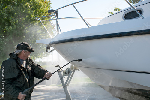 man wearing black waterproof suit while pressure washing boat hull
