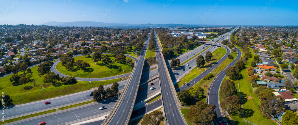 Fototapeta premium Straight road passing through interchange and leading to mountains in the distance. Aerial view in Melbourne, Australia