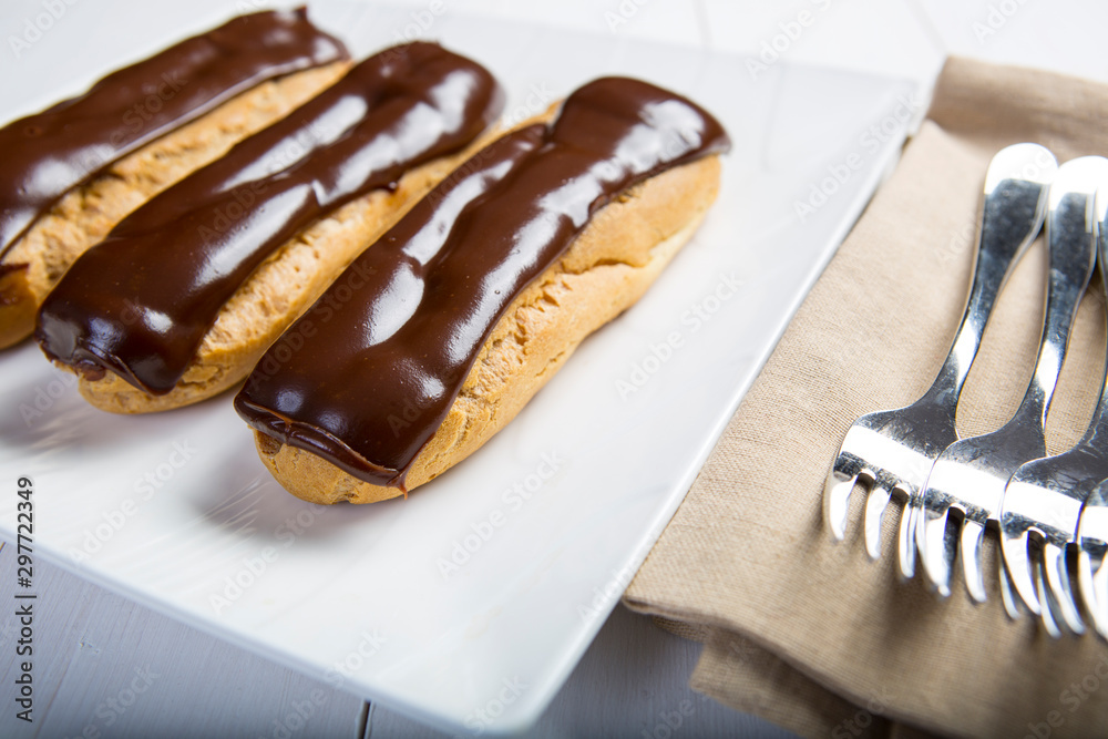 Chocolate eclair, filled with fresh whipped cream and topped with chocolate icing on a white plate Chocolate eclair, filled with fresh whipped cream and topped with chocolate icing on a white plate