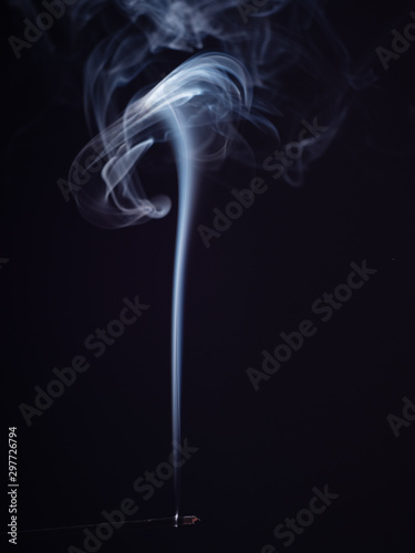 Aromatic stick burning with white smoke, isolated on black background, close up view. Structure of white smoke, brush effect. Abstract background. Sweet smell for meditation and relaxation